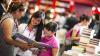 Mujer y dos niñas comparten libro mientras visitan feria de literatura